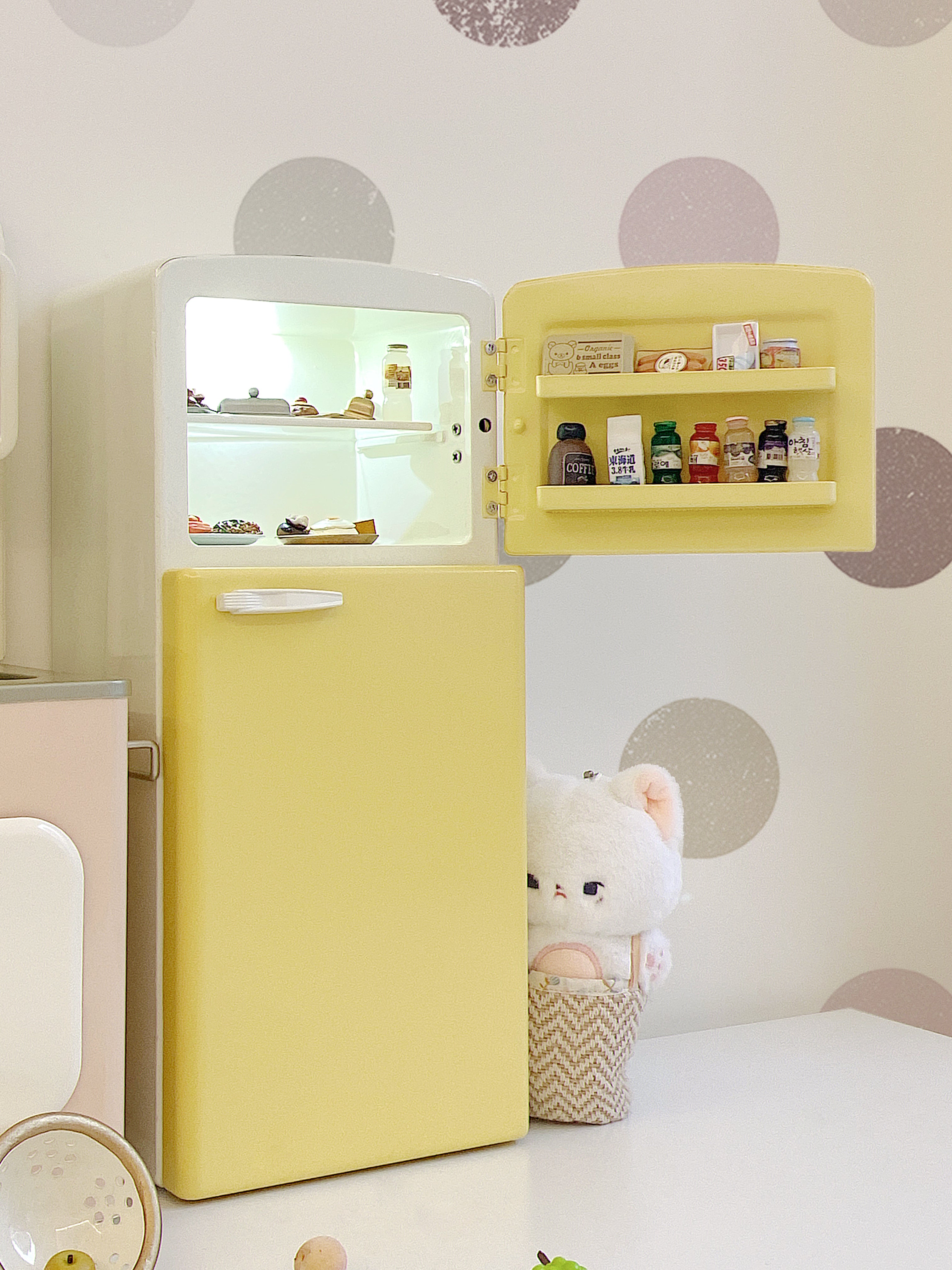 Close view of open yellow dollhouse refrigerator with lit upper shelf and door storage food props