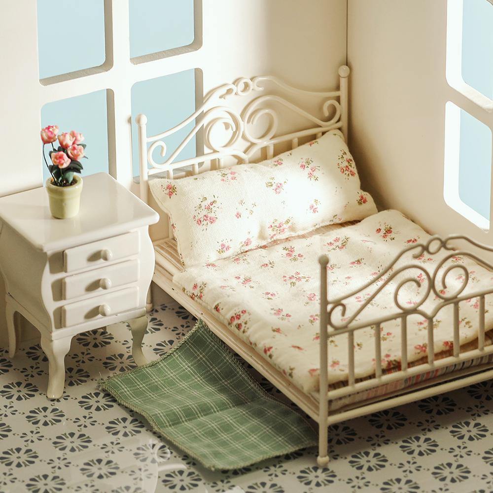 Close-up of white 1:12 dollhouse antique bed with floral bedding and curved wire scrollwork