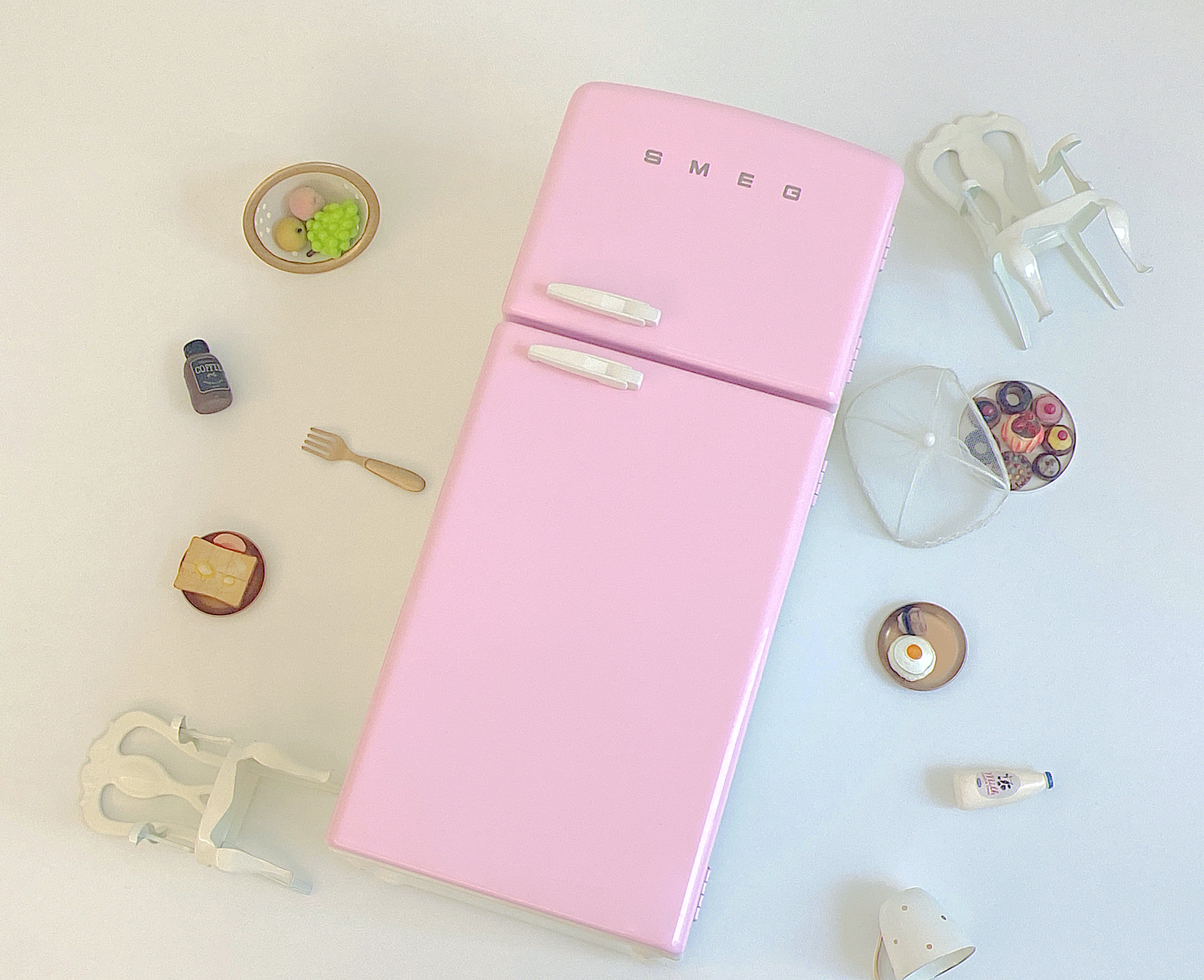 Closed pink dollhouse refrigerator shown from above with chairs, dishes and miniature food props not included